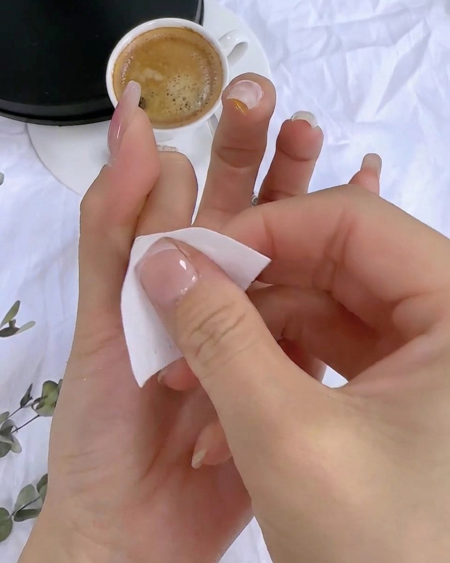 Eine Hand reinigt mit einem fusselfreien Tuch die klebrige Rückstandsfläche des ausgehärteten Nagels.