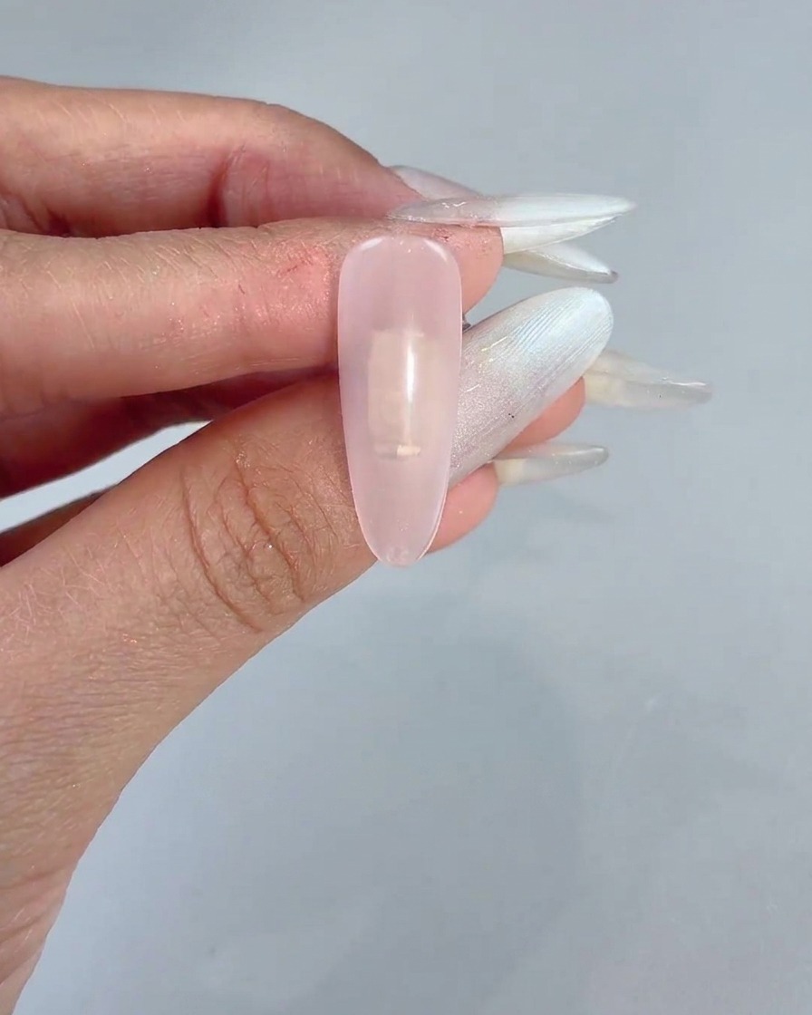 Ein Schwammblock tupft sanftes rosafarbenes Gel auf die Mitte eines klaren Nagels.