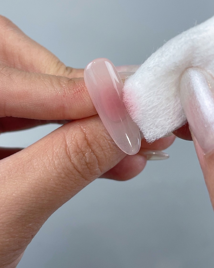 Eine Hand tupft mit einem weißen Schwammblock rosafarbenes Gel auf die Mitte eines klaren, mandelförmigen Nageltips.