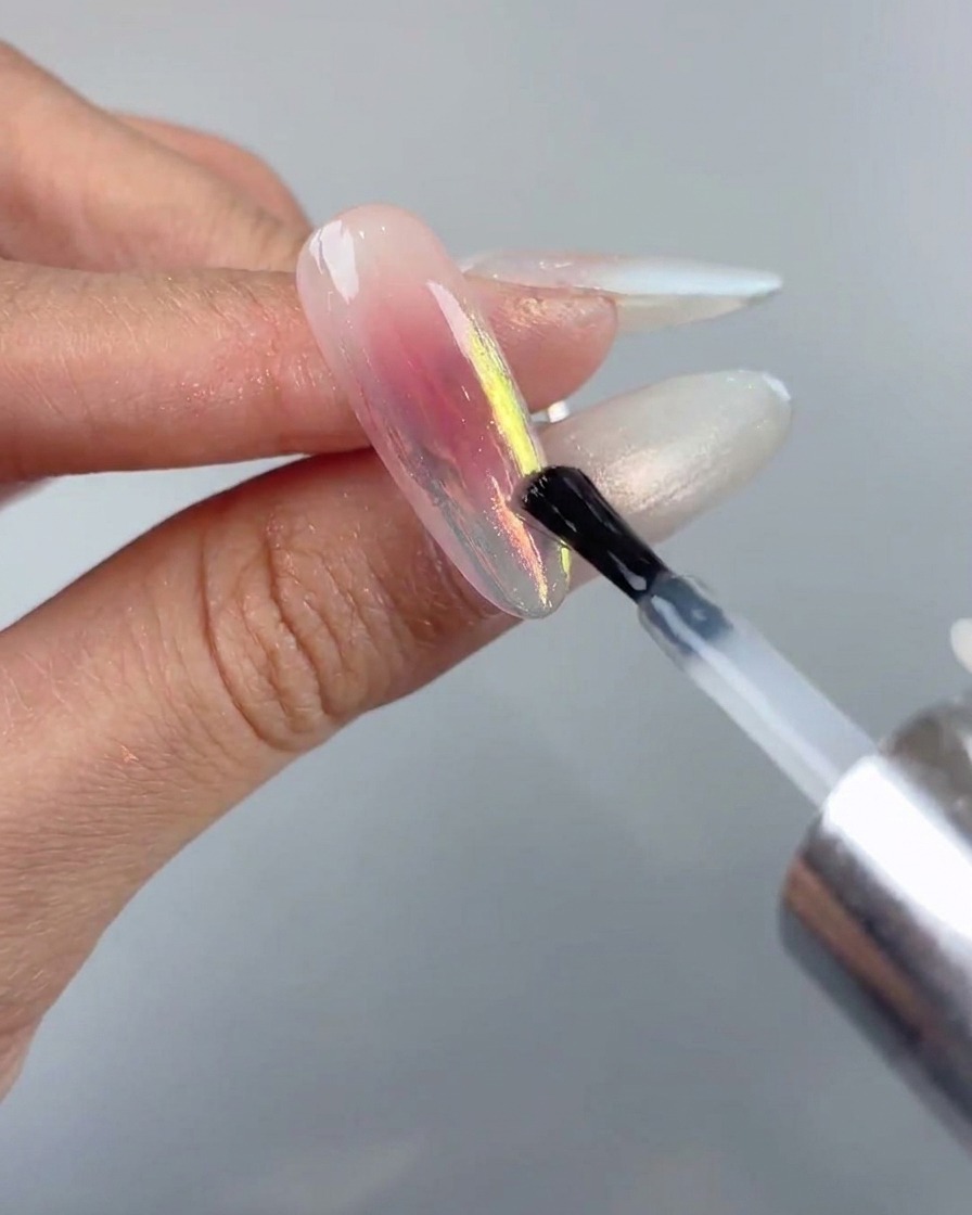 Ein Nagelpinsel trägt eine letzte versiegelnde Top-Coat-Schicht über einem Aurora-Chrome-Nageldesign auf.