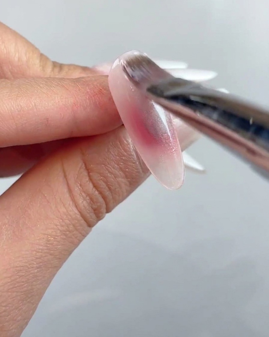Ein Nagelpinsel trägt eine Schicht klares Cat-Eye-Gel über die gesamte Oberfläche des vorbereiteten Nagels auf.