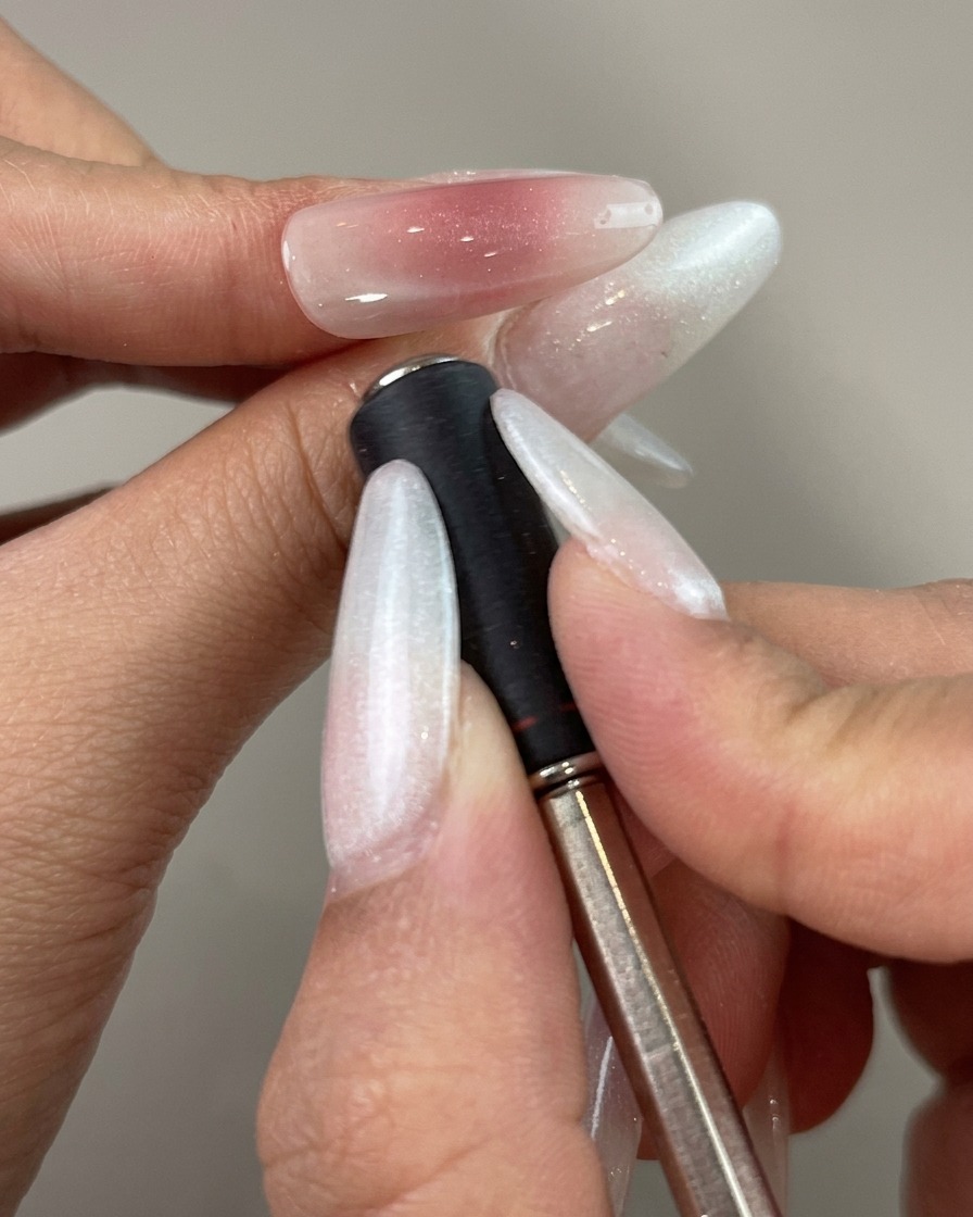Ein Magnetstab wird nah an die Seite eines lackierten Nagels gehalten, um eine geschwungene Reflexionslinie zu formen.
