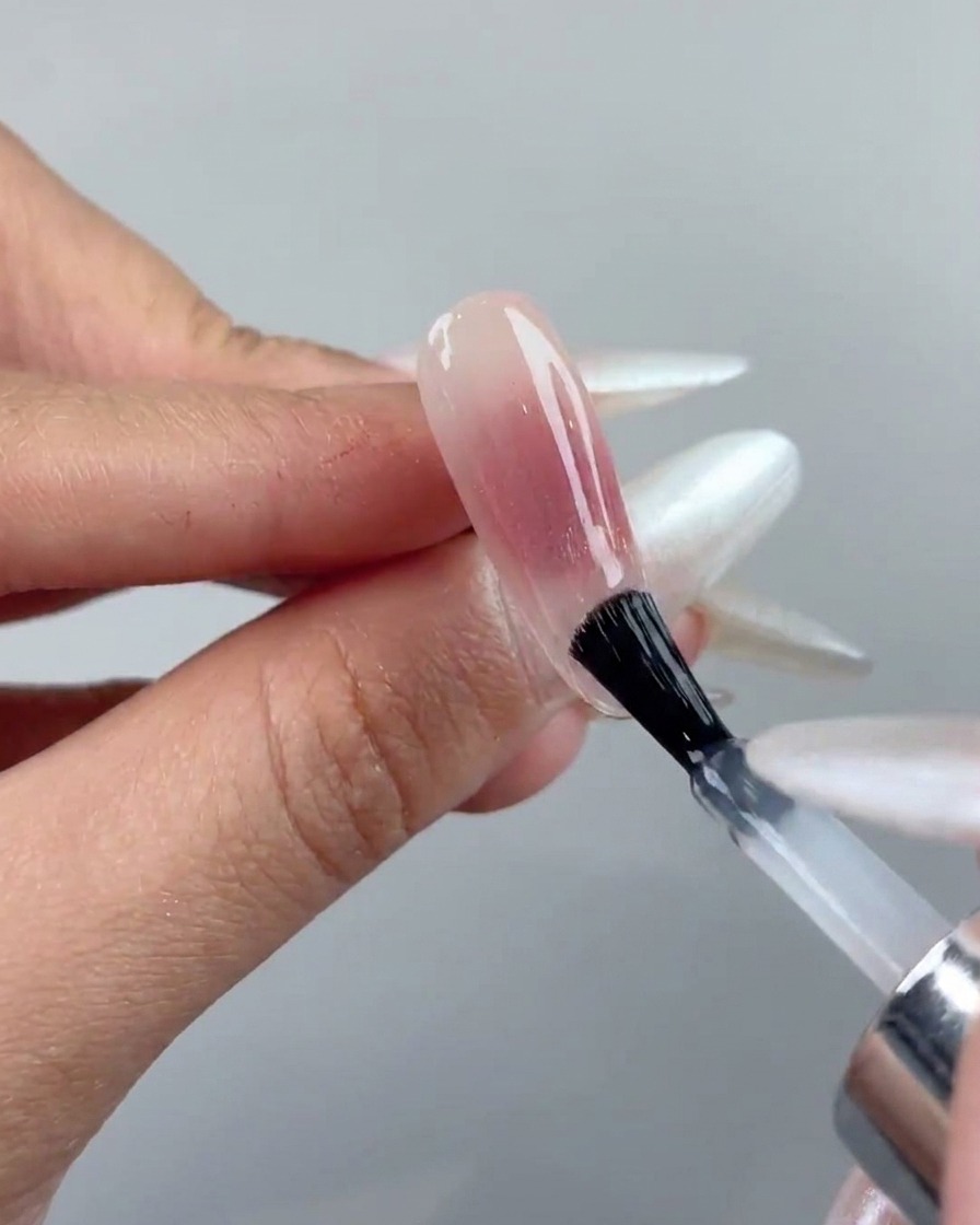 Ein Nagelpinsel trägt eine klare Top-Coat-Schicht über einem ausgehärteten Cat-Eye-Gel-Nagel auf.
