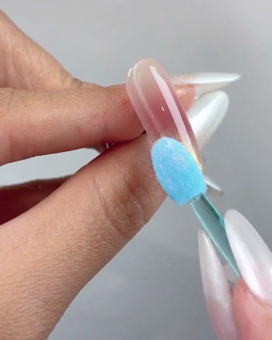 Ein blauer Silikonschwamm-Applikator presst Aurora Chrome Powder auf die Nagelspitze.