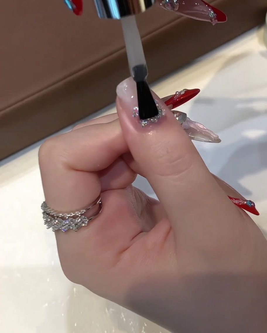 Ein flacher Gelpinsel trägt eine dicke Schicht klares Aufbaugel über einem Nagel mit eingekapseltem Glitzer auf.