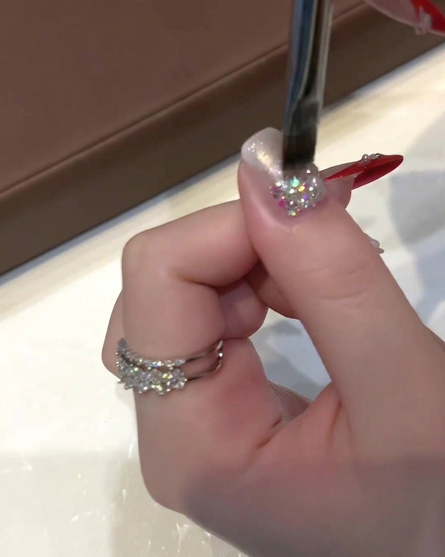 Eine Hand hält einen flachen Gelpinsel und trägt durchscheinenden Cat-Eye-Lack auf einen glitzernden Nagel auf.
