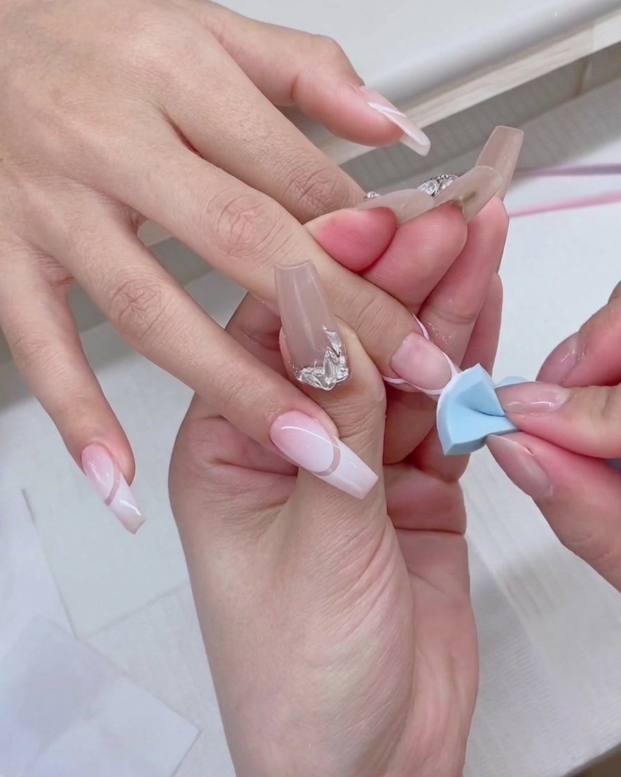 Ein blauer Make-up-Schwamm wird sanft auf die Spitze eines Fingernagels getupft, um einen weißen Gradient-Effekt zu erzeugen.