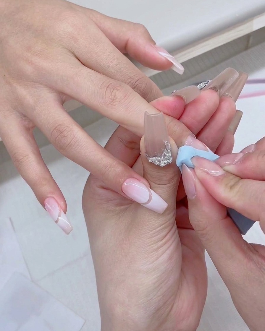 Ein Gel-Nagellackpinsel trägt frisches weißes Produkt direkt auf die Kante eines blauen Make-up-Schwamms auf.