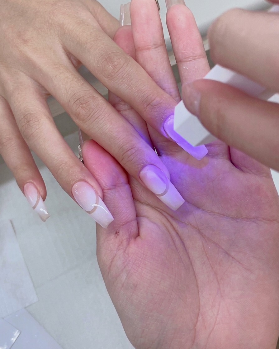 Eine Hand ruht in einer rosa UV/LED-Nagellampe, während violettes Licht die vorbereiteten Gradient-Nägel erhellt.