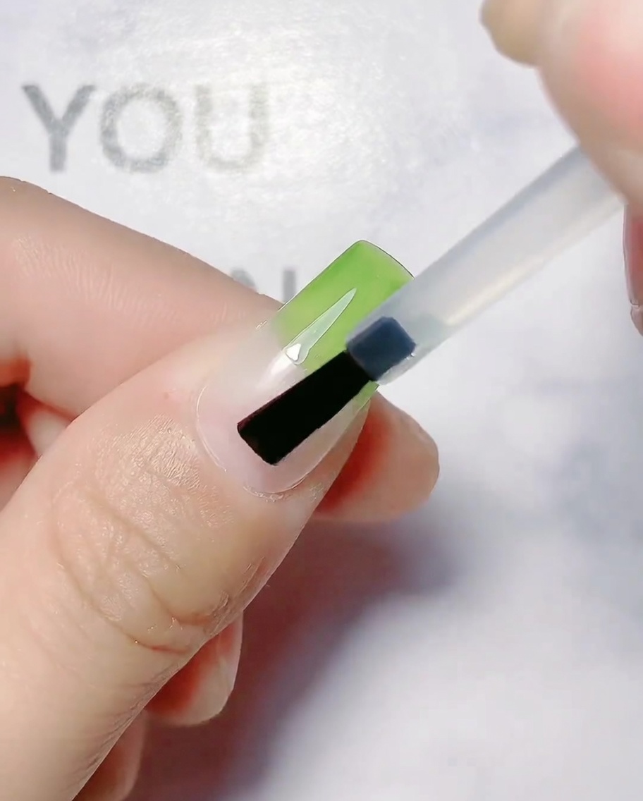Ein Nagelpinsel trägt olivgrünes Gel auf die obere Hälfte eines Naturnagels auf.