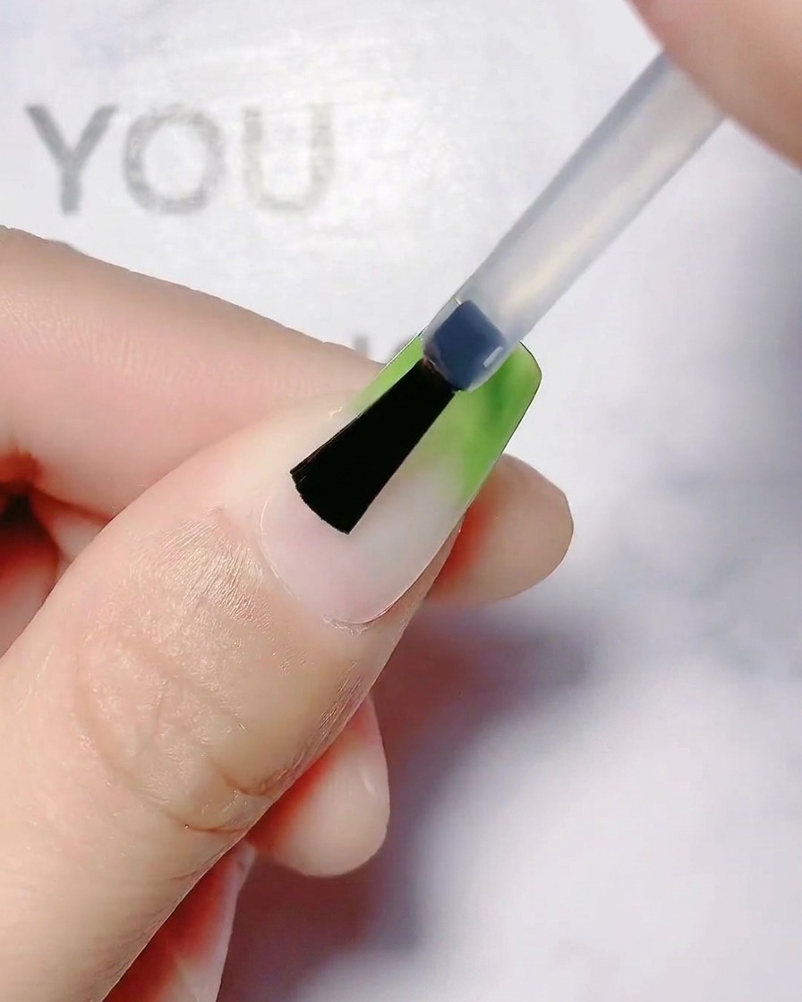 Ein Pinsel glättet den olivgrünen Farbverlaufsübergang auf einem Fingernagel.