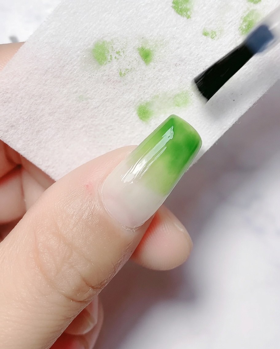 Ein Reinigungspad wischt die klebrige Inhibitionsschicht von einem ausgehärteten Nagel mit Farbverlauf ab.