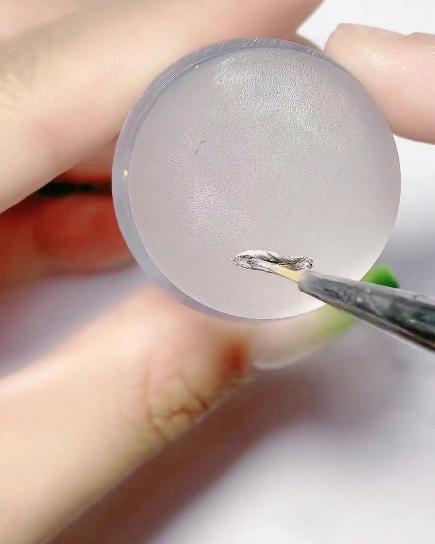 Ein feiner Pinsel trägt silbernes Gel auf die flache Oberfläche eines Silikonstempelkissens auf.