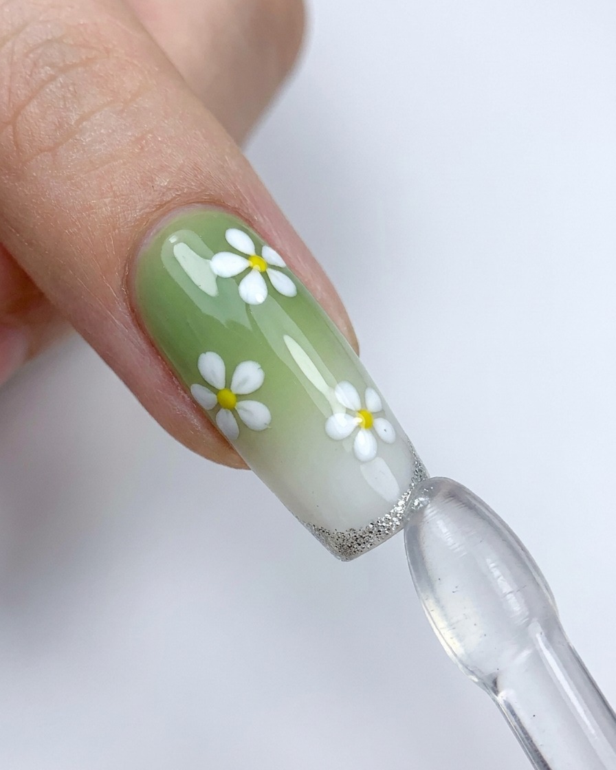 Ein dekorierter Nagel mit weißen Blumen wird gegen einen Silikonstempel gedrückt, um eine silberne French-Spitze aufzutragen.