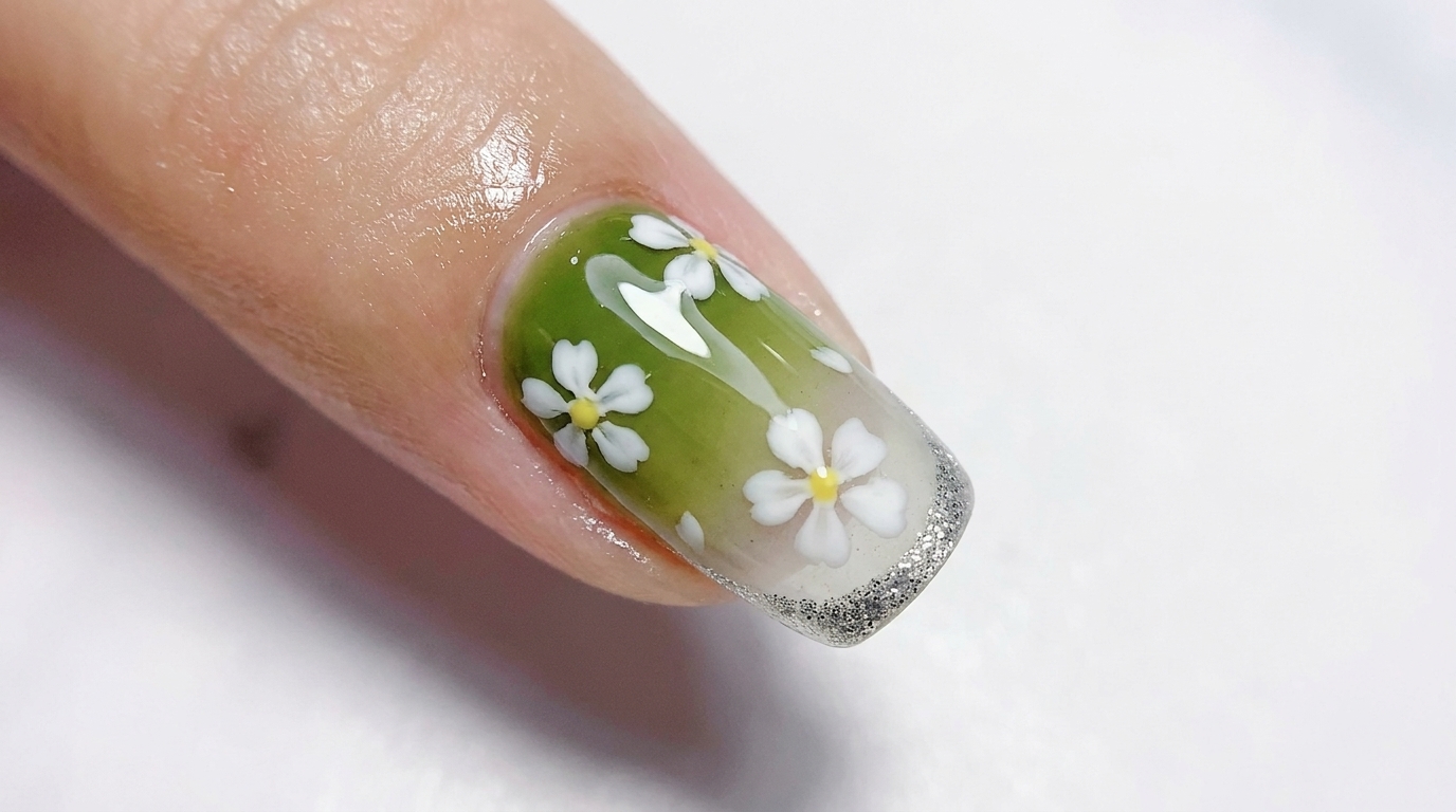 Glänzender Nagellack mit einem Farbverlauf von Olivgrün zu transluzentem Weiß, verziert mit klaren weißen fünfblättrigen Blumen und einer feinen Silberglitter-French-Spitze.