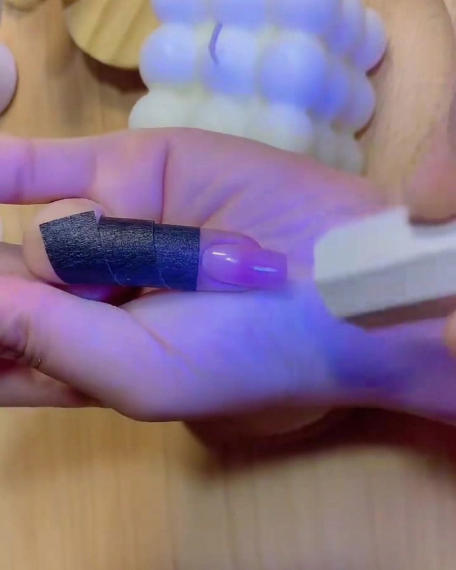 Eine Hand in einer UV/LED-Nagellampe positioniert, mit blauem Licht, das die Finger und den ausgehärteten Farbverlaufs-Nagel beleuchtet.