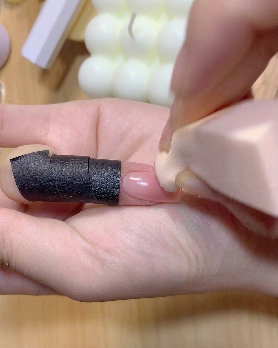 Ein Make-up-Schwamm tupft rosa Farbe auf einen manikürten Fingernagel, um den Ombré-Farbverlauf zu intensivieren.