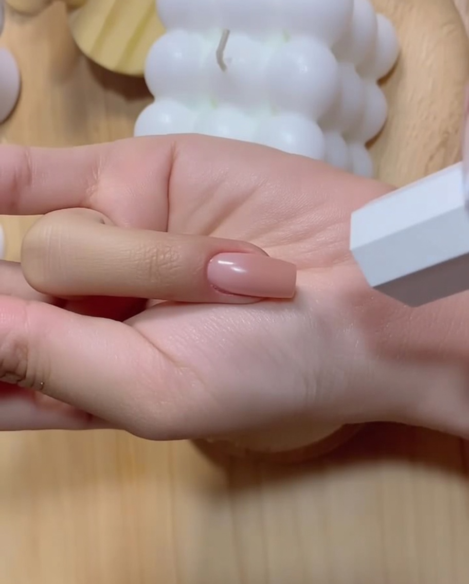 Ein manikürter Hand mit einem vertieften rosa Farbverlaufs-Fingernagel, der in der Nähe einer weißen UV-Lampe positioniert ist.