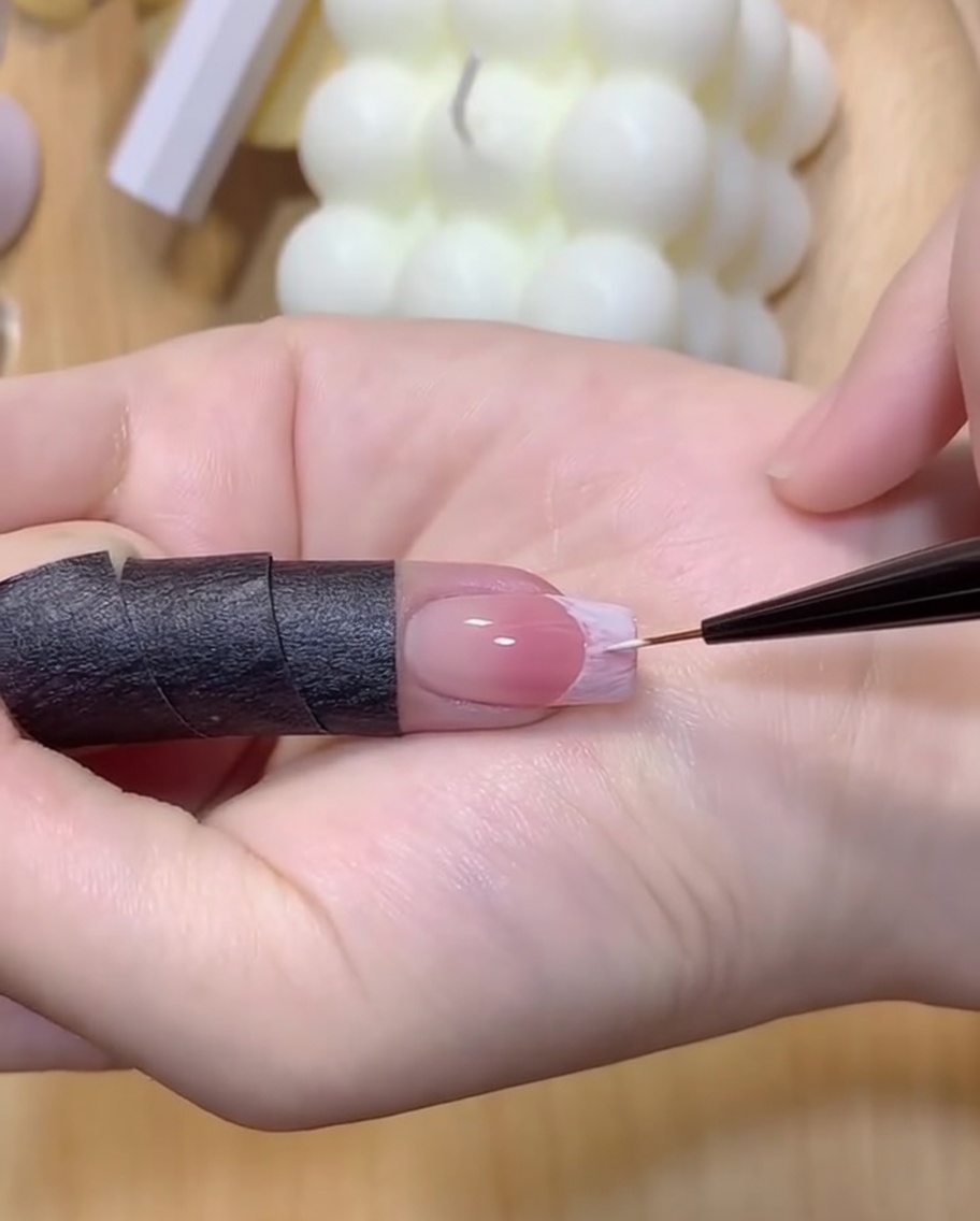 Eine Hand unter einer UV/LED-Lampe härtet die frisch umrissene weiße French-Nagelspitze aus.