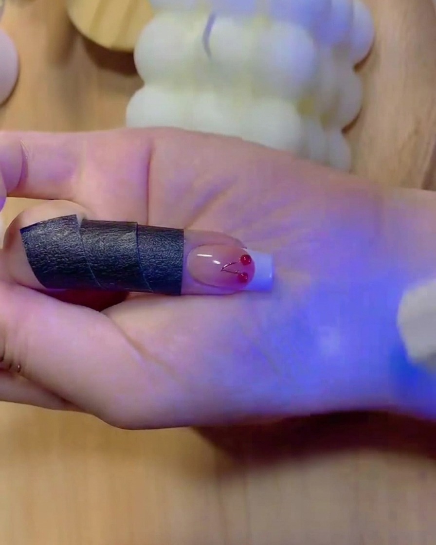 Ein feiner Pinsel füllt die solide weiße Farbe einer French-Maniküre-Spitze auf einem Ombré-Nagel aus.