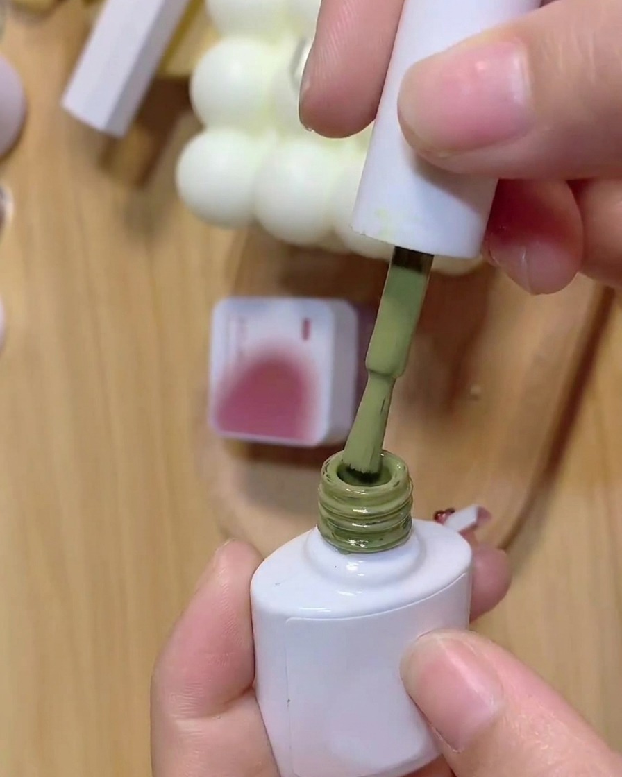 Ein Pinsel taucht in eine Flasche grünes Gel mit einem Hintergrundglas aus rosa Gel.