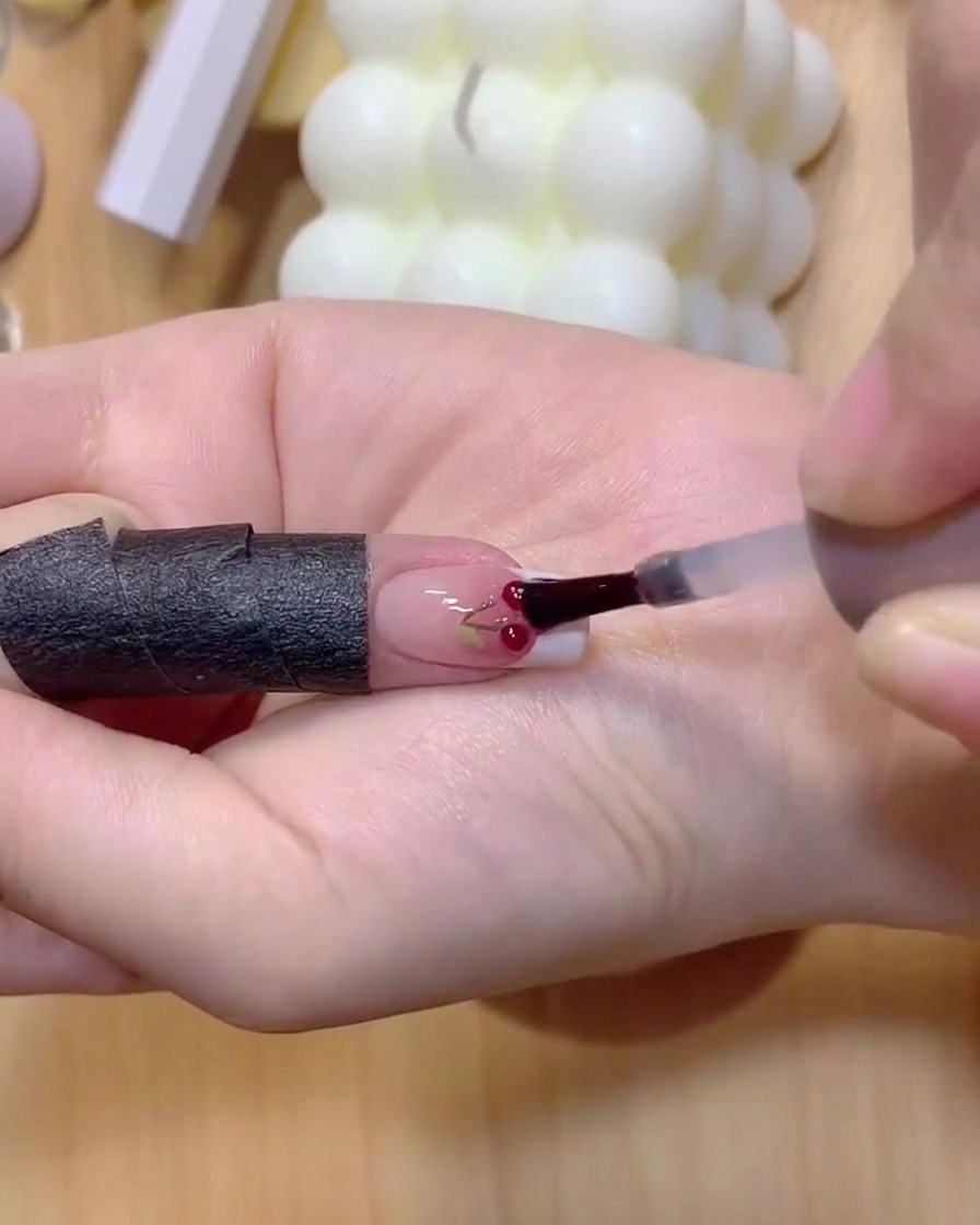 Ein Fingernagel mit gemalten Kirschstielen wird unter eine Härtungslampe gelegt.