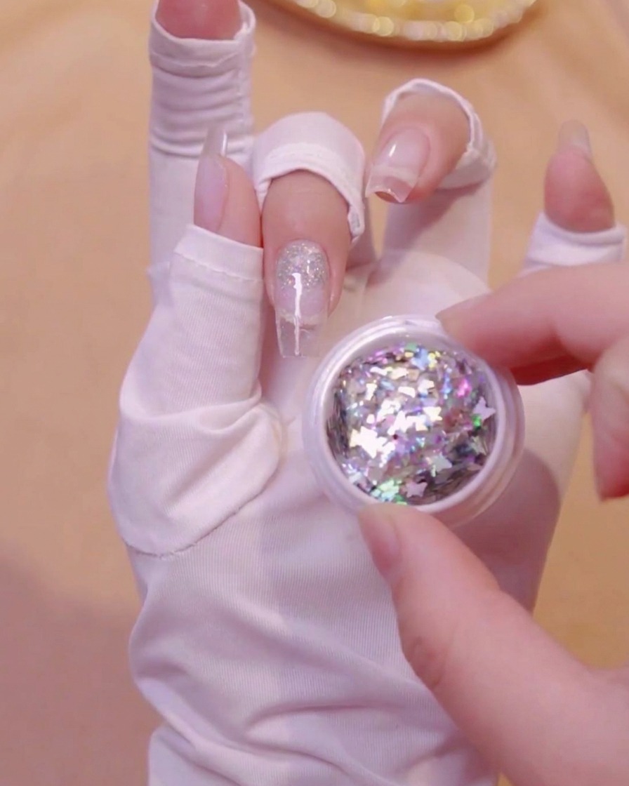 Eine Hand hält ein geöffnetes, kleines Glas gefüllt mit holografischen Schmetterlingsglitter-Pailletten.