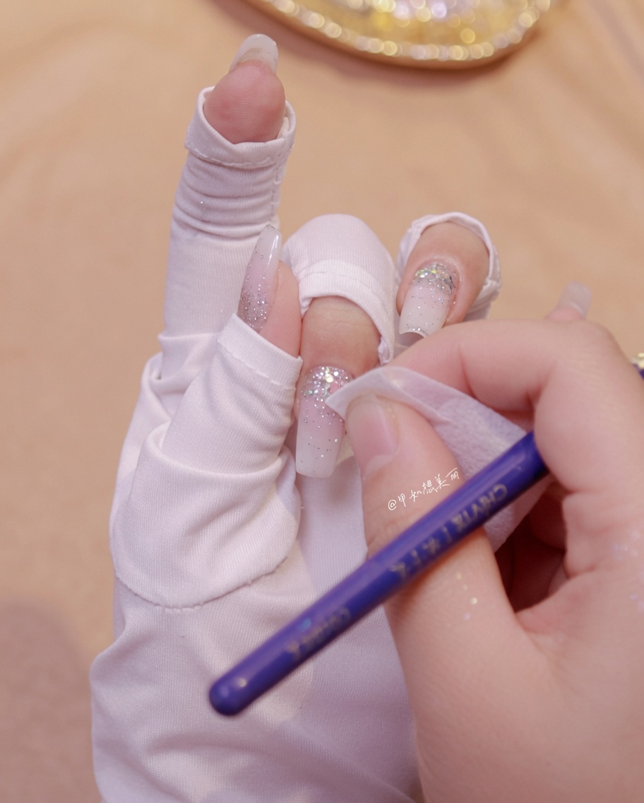 Eine Hand reinigt mit einem Tuch den Bereich um die Schmetterlingsglitter-Dekorationen auf einem manikürten Nagel.