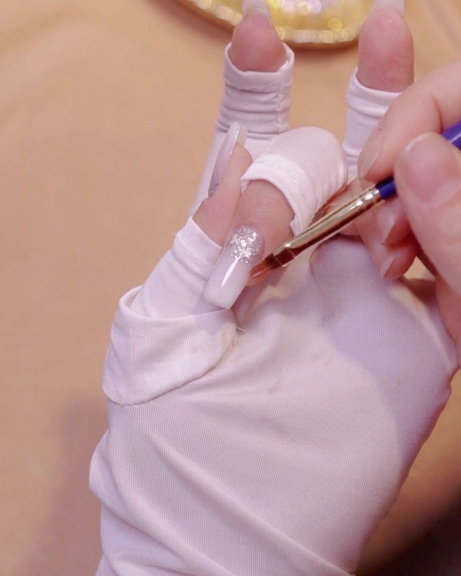Ein Gradientenpinsel glättet die zweite Schicht milchweißen Gels auf einem Nagel.