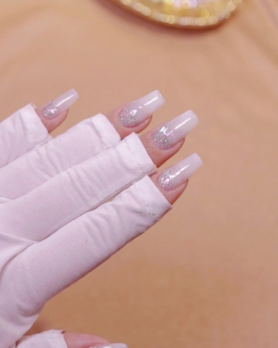 Eine Hand in einer UV-LED-Nagellampe härtet die milchweiße Gradienten-Schicht aus.
