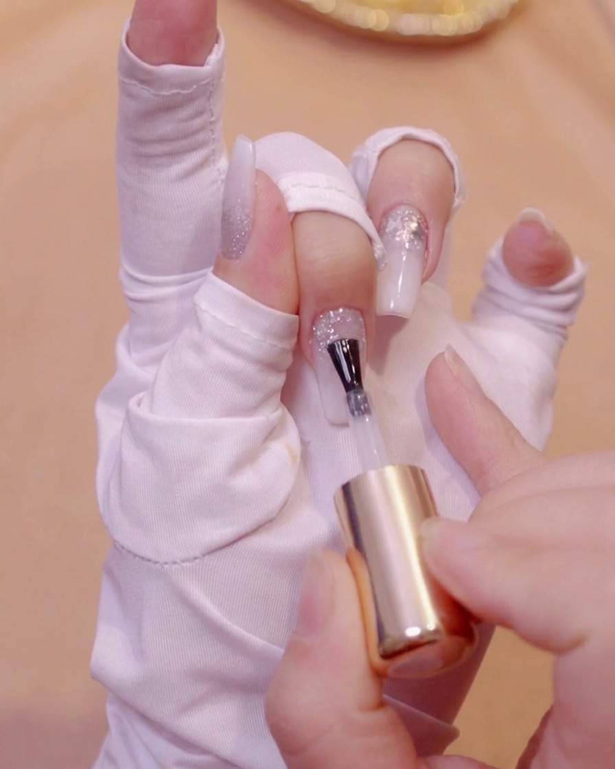 Ein Pinsel trägt klares Niveliergel auf eine texturierte Glitter-Nageloberfläche auf.