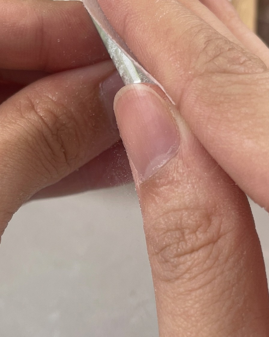 Finger verwenden eine weiße, fusselfreie Zellette, um die klebrige Schwitzschicht von einem frisch ausgehärteten, klaren Gelnagel zu entfernen.