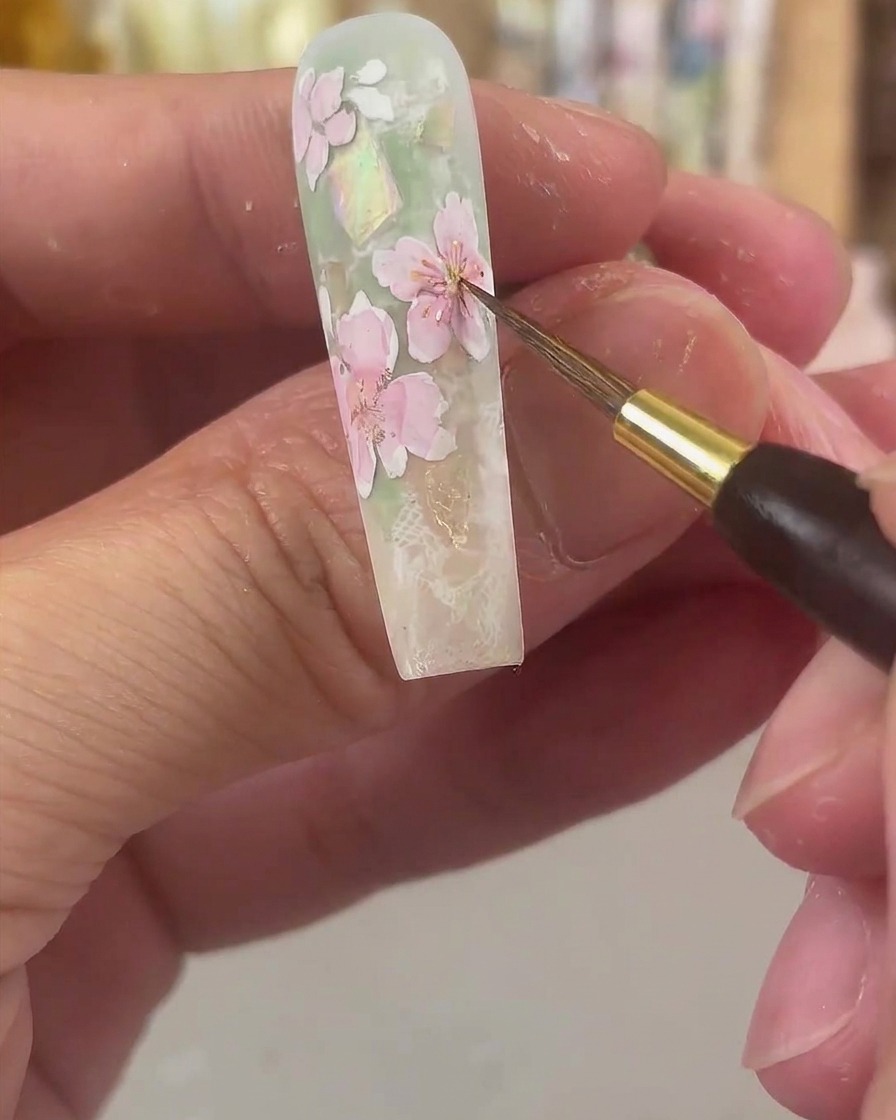 Ein feiner Detailpinsel tupft leuchtend gelbe Aquarellfarbe in die Mitte der rosa getönten Blütenblätter.