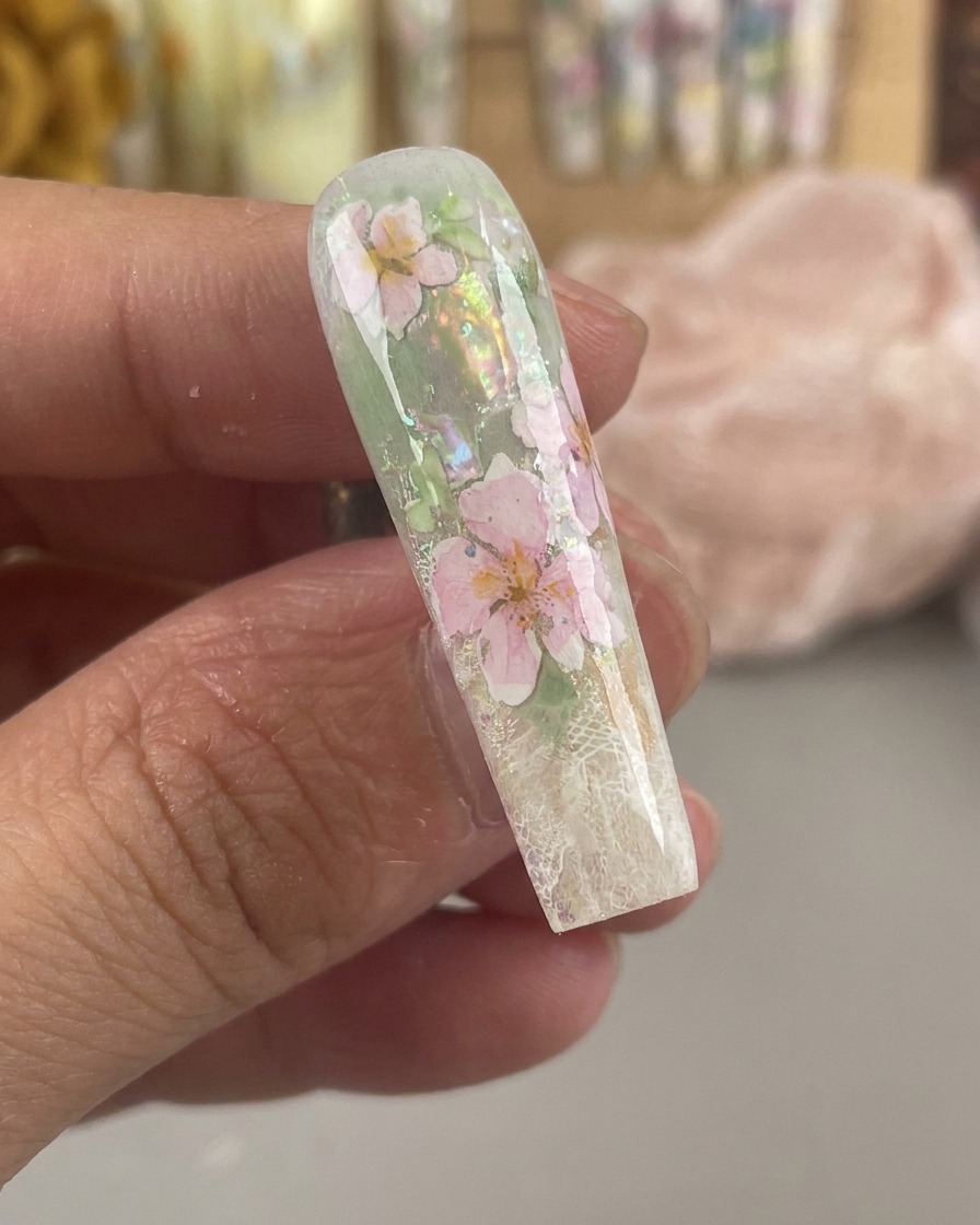 Ein glänzender, eingekapselter Nagel, der versiegelte rosa und gelbe Aquarellblumen unter einer dicken, klaren Gelschicht zeigt.