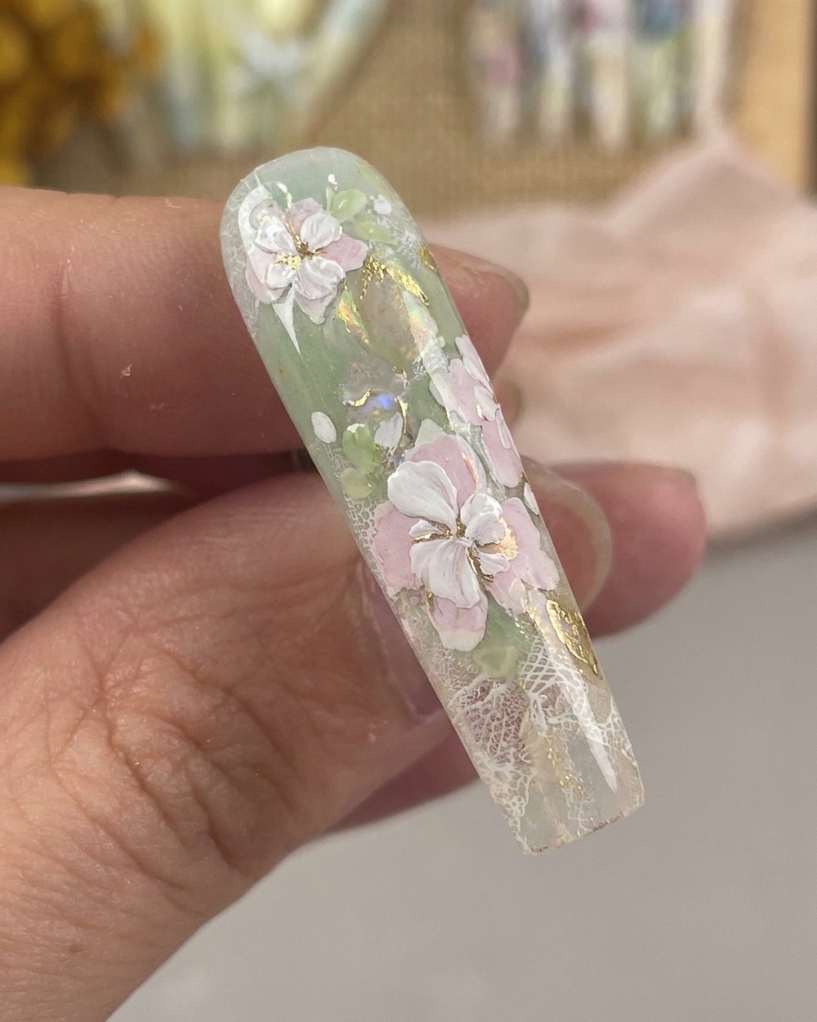 Nahaufnahme eines ultrafeinen Nail-Art-Pinsels, der zarte weiße Staubgefäßdetails und mittlere Punkte auf einem Blumendesign zeichnet.