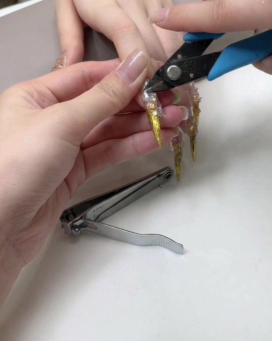 Ein Nagelknipser, der die scharfe spitze Spitze einer langen metallischen Nagelverlängerung abschneidet.