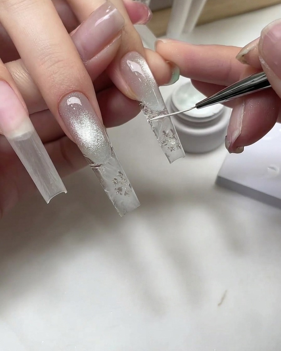 Ein feiner Nailart-Pinsel zeichnet weiße Schneeflockendetails auf eine klare, strukturierte Nagelverlängerung.