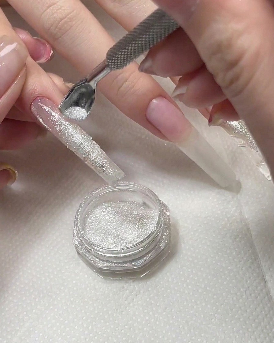 Ein Pinsel fegt überschüssiges Diamantpulver von einer ausgehärteten Nageloberfläche weg.