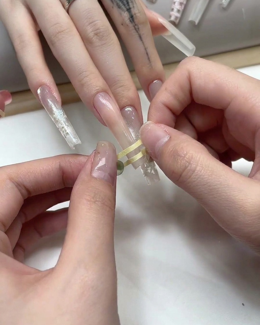 Finger platzieren feines goldenes Striping-Tape in einem Gittermuster auf einem nudefarbenen Gelnagel.