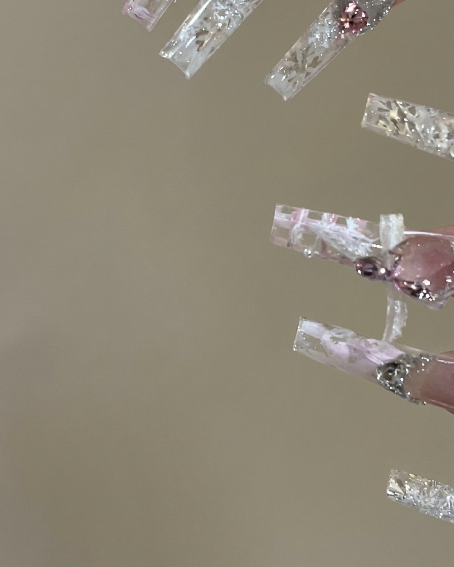 Eine Nageldesignerin trägt Top-Coat auf und streicht vorsichtig farbiges Gel in die Gitterbereiche eines Karo-Nageldesigns.