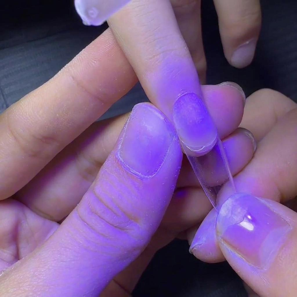 Ein Fingernagel mit klarem Tip wird für ein schnelles Anhärten unter eine lila UV-Lampe gehalten.