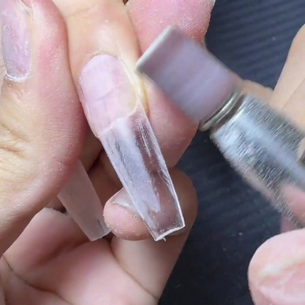 Ein Fräser mit lila Schleifband glättet den Übergangsbereich zwischen Verlängerungs-Tip und Naturnagel.