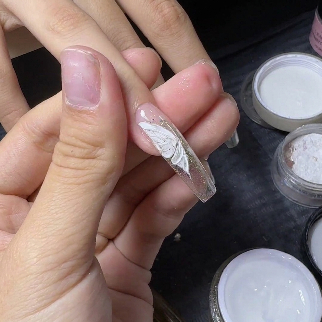 Der Daumen einer Nageldesignerin hält einen Nagel, um einen kleinen silbernen Strassstein zu befestigen.