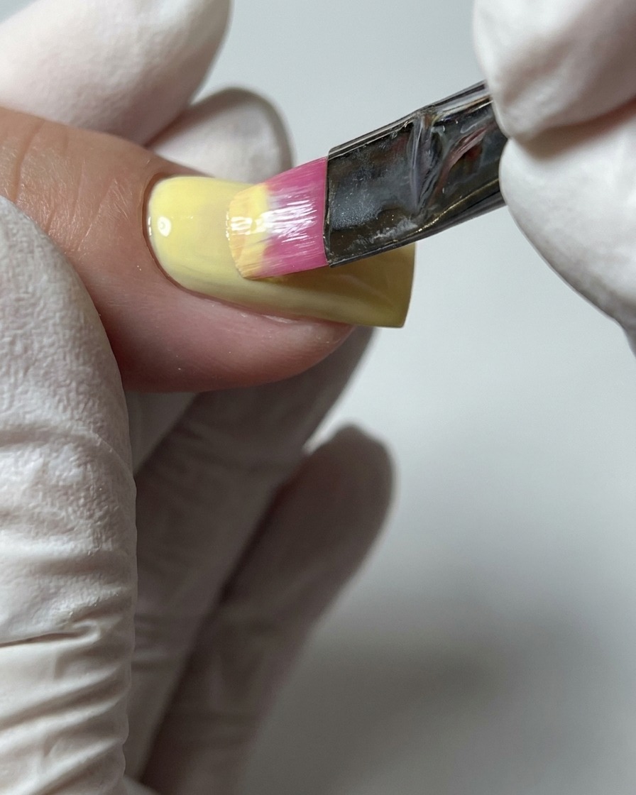 Eine Nahaufnahme eines Pinsels, der eine zweite Schicht pastellgelben Gelacks aufträgt, um vollständige Farbdeckung zu erzielen.