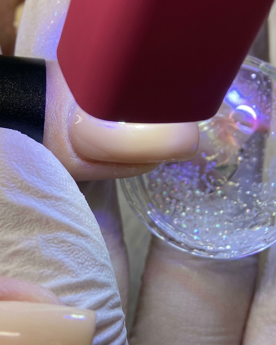 Eine rote UV/LED-Handlampe strahlt Licht auf einen Fingernagel, um ein mit Glitzer überzogenes weißes Stern-Design auszuhärten.