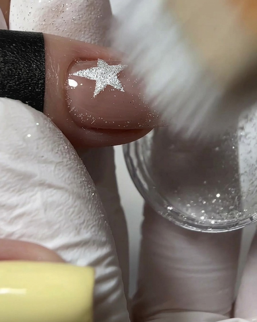 Ein fester Pinsel fegt überschüssiges silbernes Glitzerpulver von einem strukturierten Nageldesign.