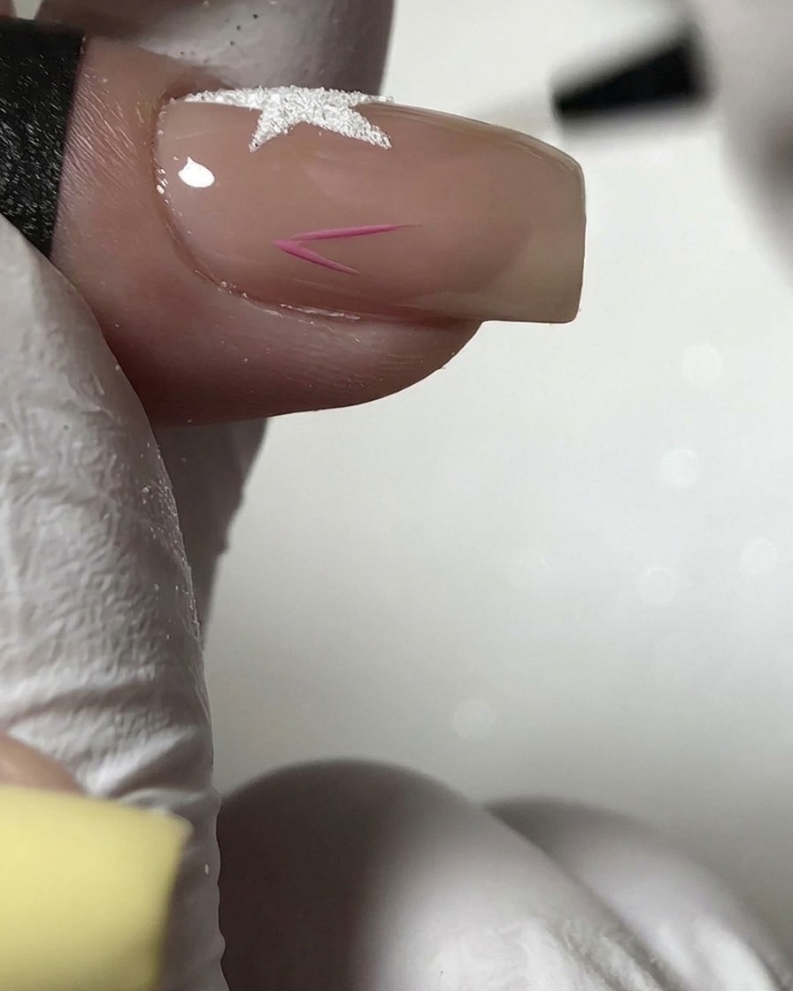 Ein feiner Pinsel malt die Umrisse eines kleinen rosa Sterns auf den unteren Bereich eines Nude-Nagels.
