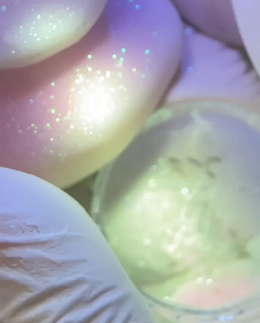 Eine handschuhbedeckte Hand hält eine Lampe über einen vorbereiteten Nagel mit einem strukturierten rosa Stern.