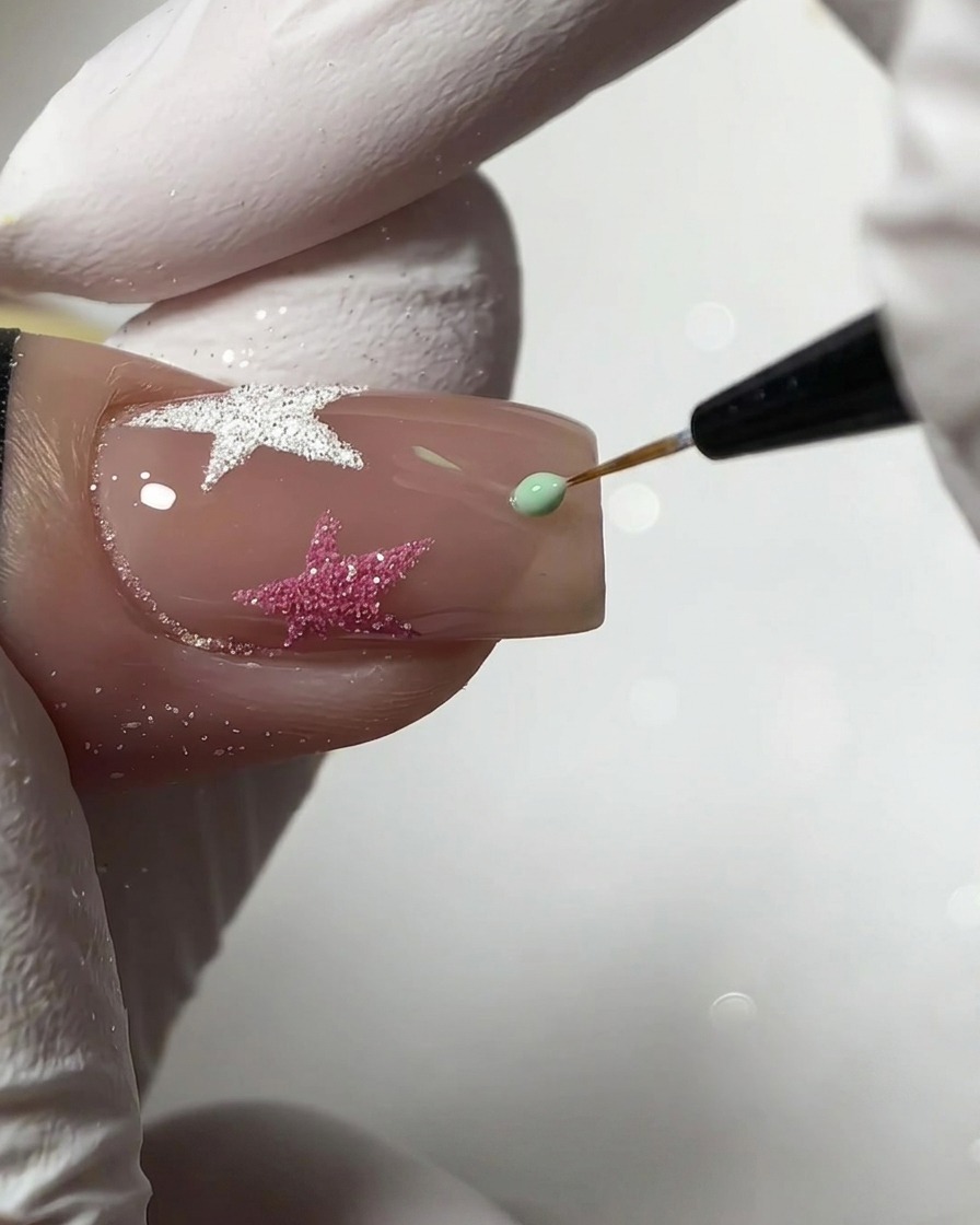 Ein feiner Liner-Pinsel trägt einen kleinen Tropfen mintgrünes Gel auf, um eine Sternform auf einem Nude-Nagel zu erstellen.