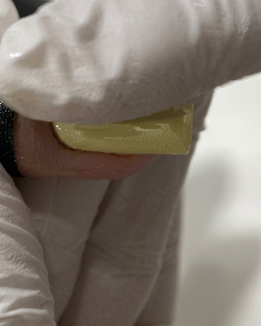Ein handschuhbedeckter Finger reibt Perl-Chrome-Pulver auf einen gelben Nagel.